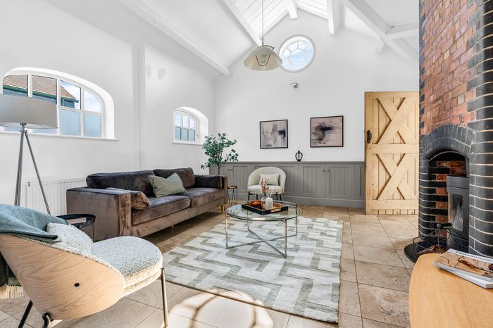 Same vaulted space staged with a velvet sofa, coffee table and wood-burning stove