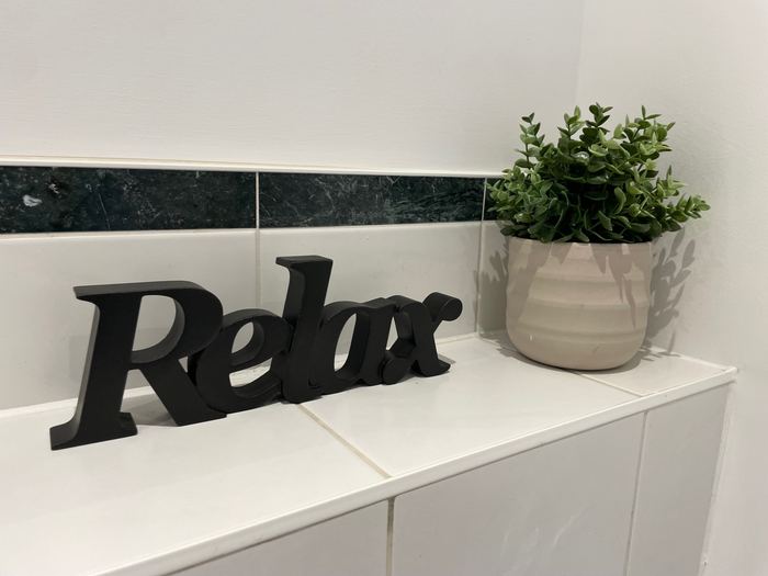 Bathroom shelf decluttering detail with a ‘Relax’ sign and potted plant