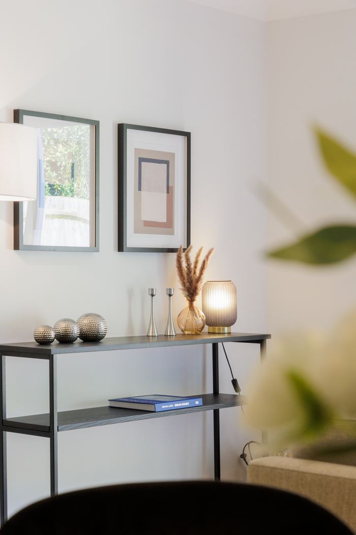Console table decluttering vignette with framed prints, candlesticks and pampas grass
