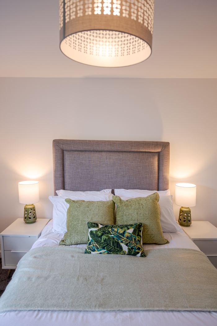 Bedroom styled with a taupe headboard and green patterned cushions