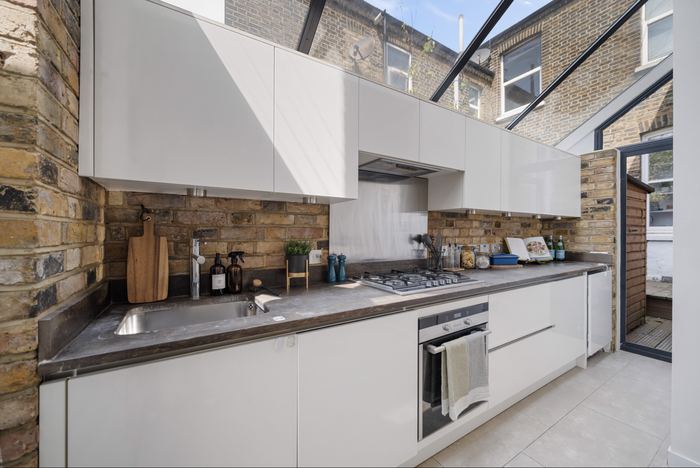 Kitchen styled with white cabinetry, a brick splashback and skylights