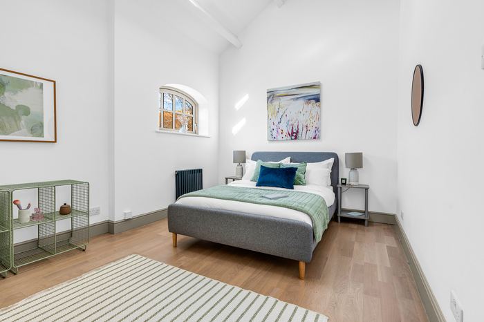 Bedroom staged with a grey upholstered bed and artwork, empty property staging