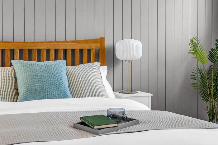 Bed headboard styling detail with a blue cushion and brass lamp